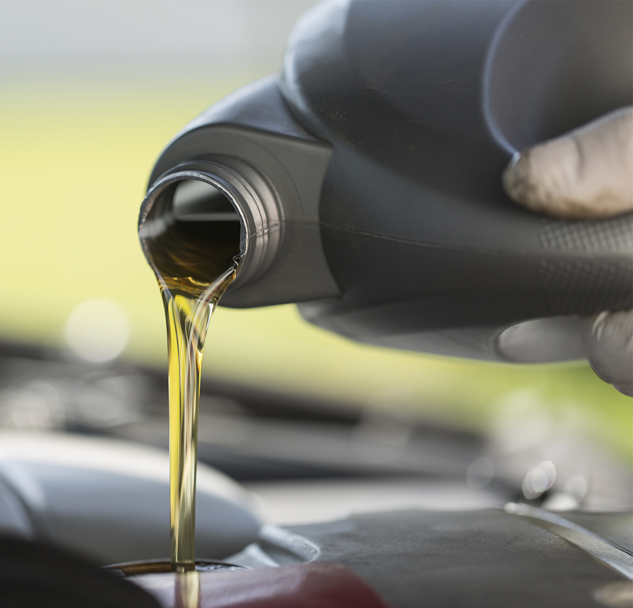 A close-up of motor oil being poured from a black container into a car engine during an oil change – BAAA Auto Service